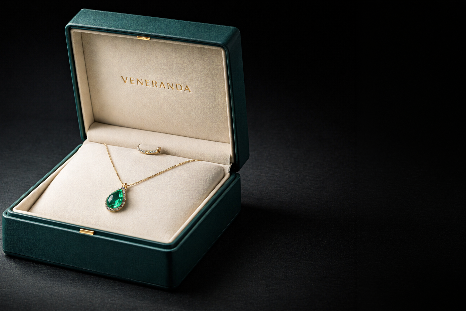 Estojo VENERANDA aberto com colar de ouro 18k e pingente de esmeralda em fundo escuro.